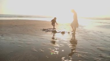 Mutlu anne ve oğul kumlu bir plajda güzel bir altın saat gün batımında birlikte oynuyorlar.