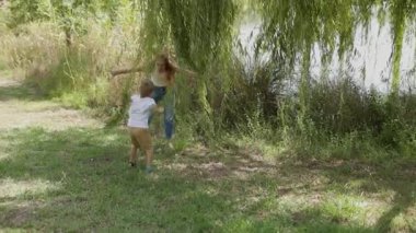 Neşeli anne ve küçük oğlu parkta bir söğüt ağacının altında kovalamaca oynuyor ve birlikte eğleniyorlar.