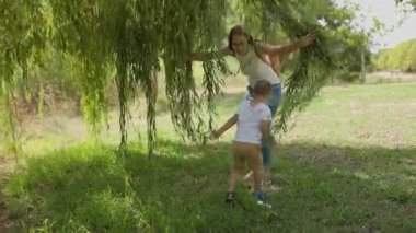 Genç ve mutlu anne ve küçük oğlu parkta birlikte oynuyorlar. Ağlayan bir söğüt ağacının altında.