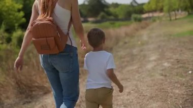 Kızıl saçlı anne ve küçük oğlu güneşli bir günün tadını çıkarıyorlar, kırsal bir yolda koşuyorlar.