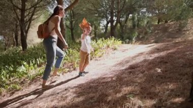 Mutlu bir aile, bir anne ve oğlu güneşli bir orman yolunda yürüyor.