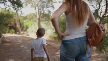 Mutlu anne ve küçük oğlu güneşli yeşil bir ormanda yürüyüş yaparak güzel bir günün tadını çıkarıyorlar.