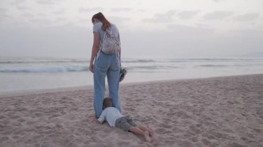 Genç anne ve küçük oğlu bir aile tatili sırasında kumlu sahilde oynarken eğleniyorlar.