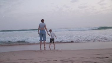 Anne ve küçük oğlu sahilde el ele tutuşup denizi izliyorlar.