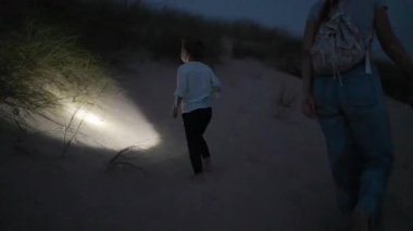 Anne ve küçük oğlu geceleri kum tepelerinde çıplak ayakla yürür, bir el feneriyle yollarını aydınlatırlar.