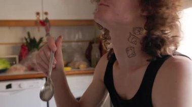 Uzun kıvırcık saçlı ergen evinde kaşıkla yemeğin tadını çıkarıyor.