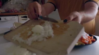 Erkek aşçı, doğradığı beyaz soğanı ahşap kesme tahtasından mutfaktaki bir tabağa koyuyor.