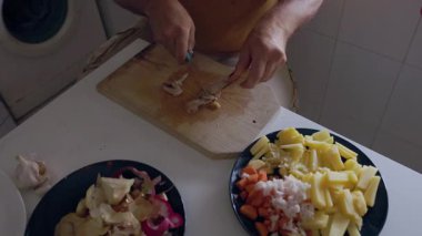 Erkek eller taze kesilmiş sebze tabaklarının yanında tahta kesme tahtasıyla et kesiyor.