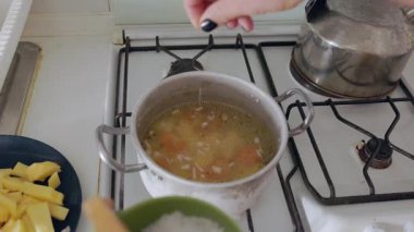 Kadın eli tuz ekliyor ve gaz sobasında ev yapımı sebze çorbası pişiriyor.