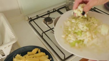 Kadın eli gaz sobasında kaynayan sebze çorbasına taze lahana ekliyor.