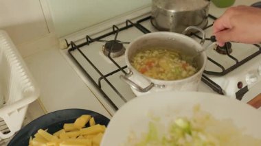 Mutfak ocağının tepesindeki kaynar çorbaya doğranmış sebze ekleyen kişi.