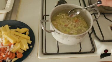 Kadın eli gaz sobasında kaşıkla haşlanmış sebze çorbasını karıştırıyor.