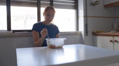 Gözlüklü kızıl saçlı kadın öğle yemeğinde sağlıklı bir salata yiyor.