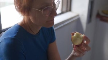 Mavi tişörtlü, sağlıklı bir atıştırmalık için olgun kırmızı elmayı yiyen genç bir kadın.