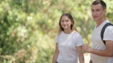 Genç bir adam ve kadın ormanda yürürken ve konuşurken el ele tutuşuyorlar.