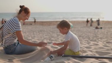 Mutlu bir aile, bir anne ve çocuğu, gün batımında kumsalda kumla oynuyorlar.