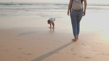 Mutlu bir aile, bir anne ve küçük oğlu, gün batımında kumlu bir sahilde çıplak ayakla yürüyorlar.