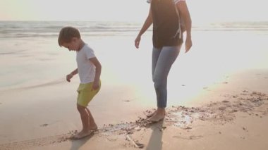 Genç bir çocuk, altın bir günbatımında annesiyle birlikte deniz kıyısında oynuyor.