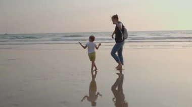 Mutlu anne ve küçük oğlu sahildeki ıslak kumda çıplak ayakla dans edip zıplıyorlar.