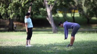 İki kadın güneşli bir parkta esneme egzersizleri yapıyor ve sağlıklı bir yaşam tarzını destekliyor.