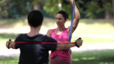 Genç bir adam ve kadın açık havada elastik bantlar kullanarak birlikte güçlü bir egzersiz yapıyorlar.