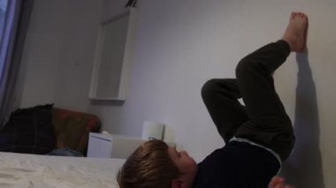 Genç enerjik bir çocuk eğleniyor, yuvarlanıyor ve yatak odasında yatağında takla atıyor.