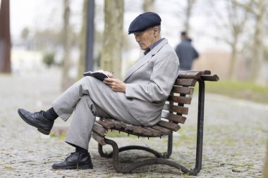 Park bankında otururken deftere yazı yazan kıdemli yazar, huzurlu bir ortamın tadını çıkarıyor.