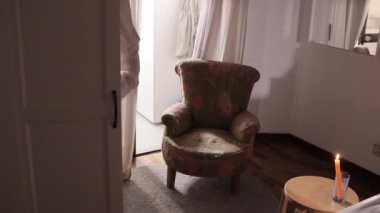 Erkek gömleği giymiş bir kadın randevuya hazırlanıyor, karanlık, rahat bir odada mum yakıyor.