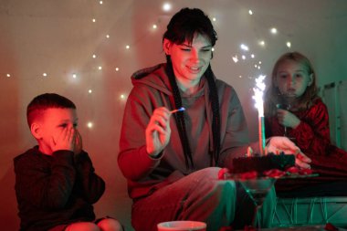 Çocuklar heyecanlı bir şekilde izlerken, annem doğum günü pastasında maytap yakıyor.