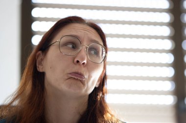 Dudakları büzüşmüş, kaşları çatık, yana bakan komik bir ifade takınan bir kadın.