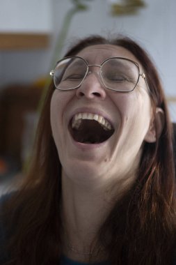 Gözlüklü kadın ağzı açık gülüyor, gerçek mutluluğu gösteriyor.