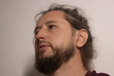 Sakallı ve uzun saçlı bir adam yukarı bakıyor, derin düşüncelerini ve duygularını gösteriyor.