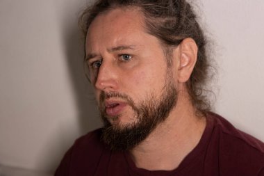 Sakallı, uzun saçlı, yana bakan, ciddi düşüncelerini ifade eden bir adam.