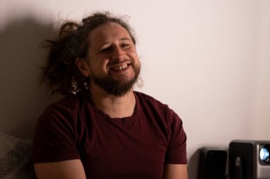 Mutlu adam evde dinleniyor, duvarda yansıtılan eğlenceli bir filmin keyfini çıkarıyor.