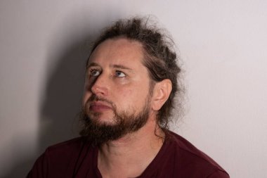 Sakallı ve kıvırcık saçlı adam yukarı bakıyor, derin düşüncelerini ifade ediyor.