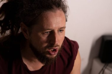 Rastalı ve sakallı bir adam aktif olarak konuşuyor ya da ağzı açık bir şekilde kendini ifade ediyor.