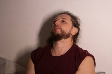 Bir adam düz bir arkaplan karşısında yukarı bakıyor, düşünüyor ya da ilham arıyor