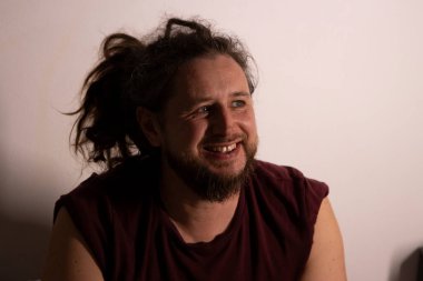 Uzun saçlı, mutlu ve arkadaşça bir ifade takınan genç bir adam.