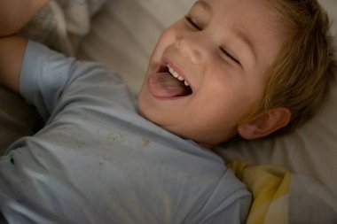 Çocuk aptal aptal bakıyor, gözleri kapalı yatakta mutlu bir şekilde yatıyor.