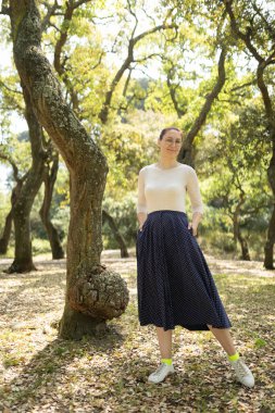 Parkta elleri ceplerinde, sıradan kıyafetler ve gözlük takan bir kadın.