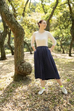 Kadın elleri ceplerinde güneşli bir parkta güneşli bir günün tadını çıkarıyor.