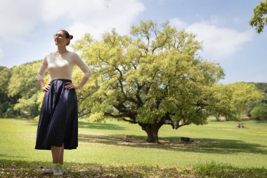 Yeşil bir parkta kendine güvenen bir kadın güneşli günün ve doğal çevrenin tadını çıkarıyor.