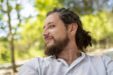 Rastgele gülümseyen sakallı adam, parkta rahatlıyor.