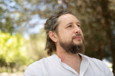 Rastalı adam yukarı bakıyor, düşünüyor ve parktaki hayatı düşünüyor.