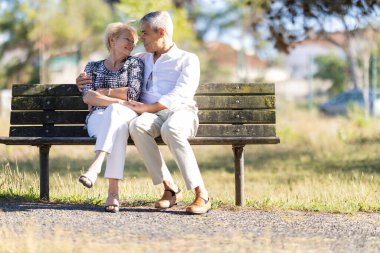 Yaşlı çift parkta bir bankta oturuyor, el ele tutuşuyorlar ve birbirlerine gülümsüyorlar.