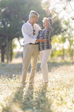Mutlu yaşlı çift, güneşli bir parkta sarılıp gülümsüyor.