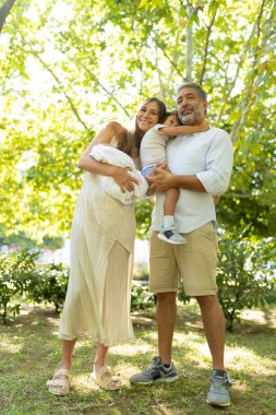 Ebeveynler iki küçük çocuklarını kucağına alıp, dışarıda mutluluklarını ve aile bağlarını ifade ediyorlar.