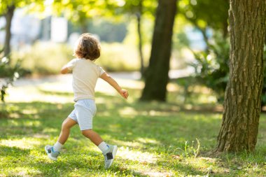 Çocuk çimenli parkta koşuyor, güneşli bir günde dışarıda oyun oynuyor.