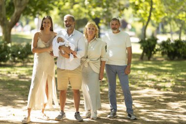 Multi-generational family standing together, celebrating the new addition to their family in a park
