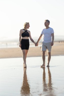 Mutlu çift, deniz kenarında çıplak ayakla yürüyüp birbirlerine bakmaktan zevk alıyor.